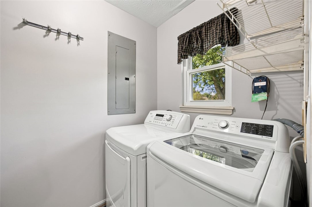 Laundry room with a white washer and dryer beneath a window and beside wall-mounted shelves.