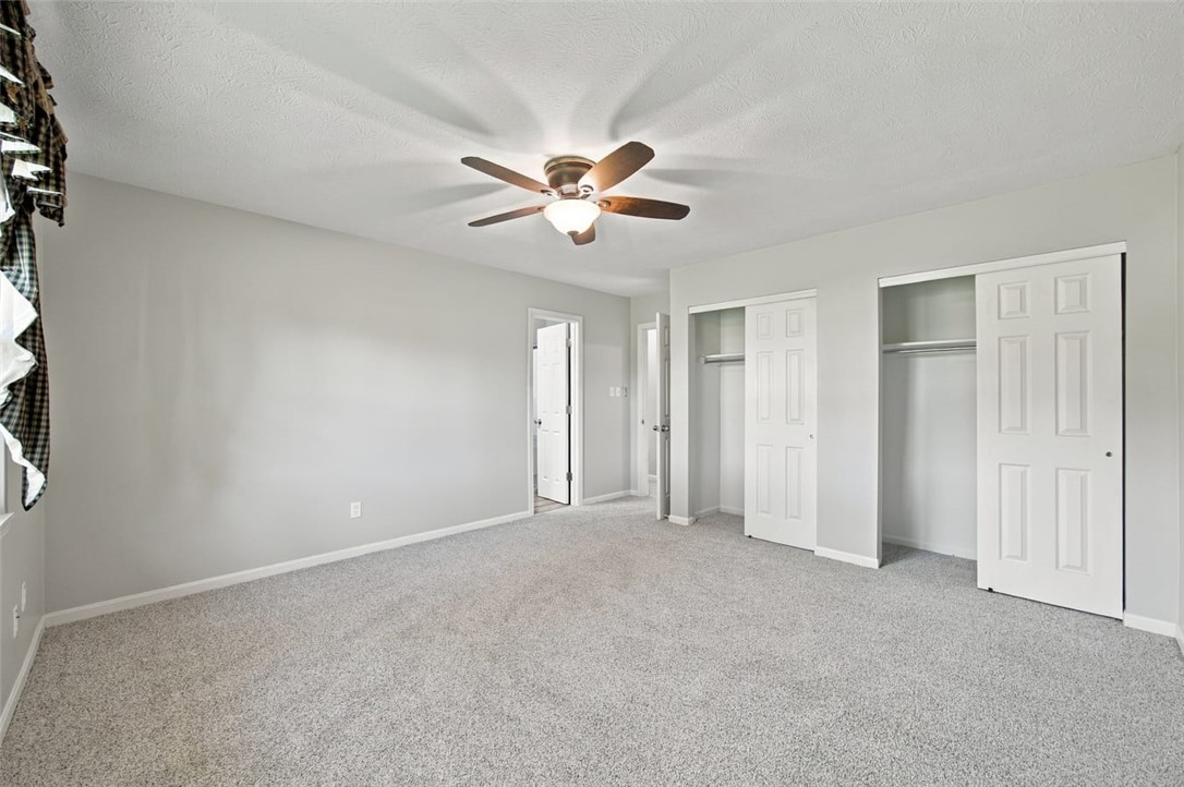 Unfurnished bedroom with gray carpet, two closets, and a ceiling fan with a light.