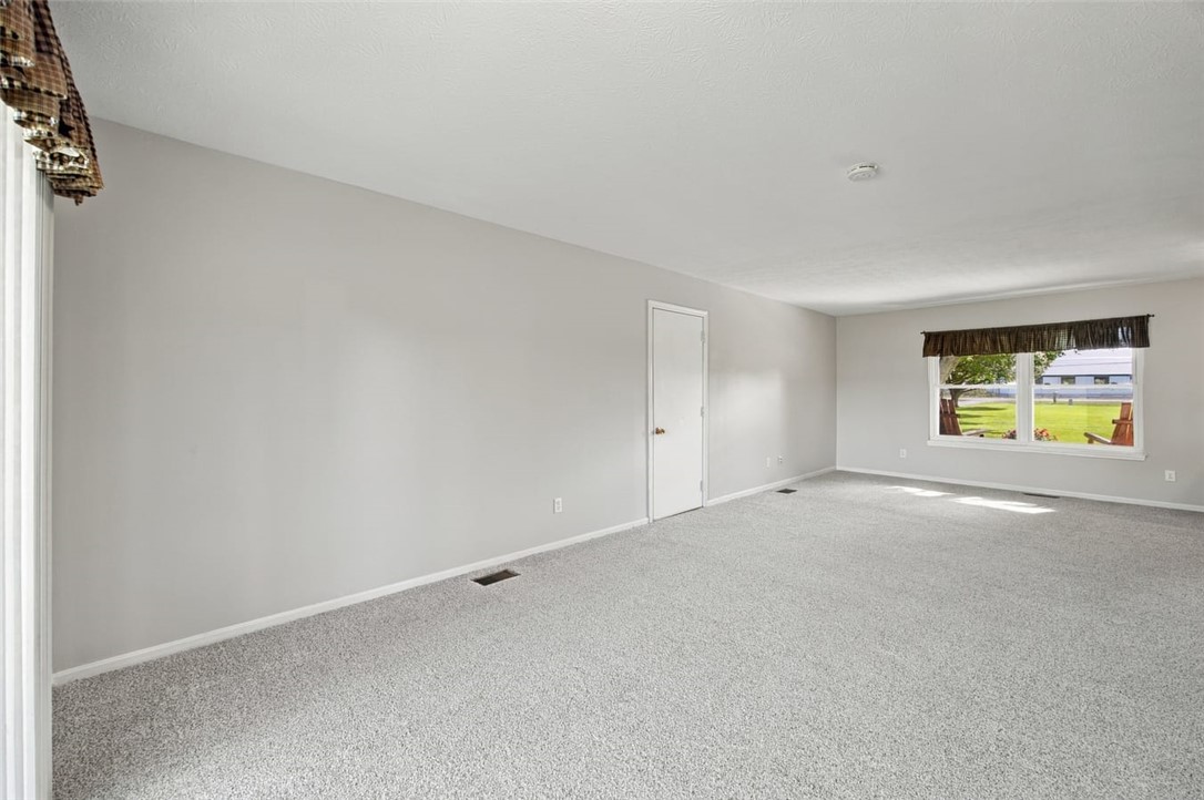 Empty carpeted room with gray walls, a window, and a closed door.