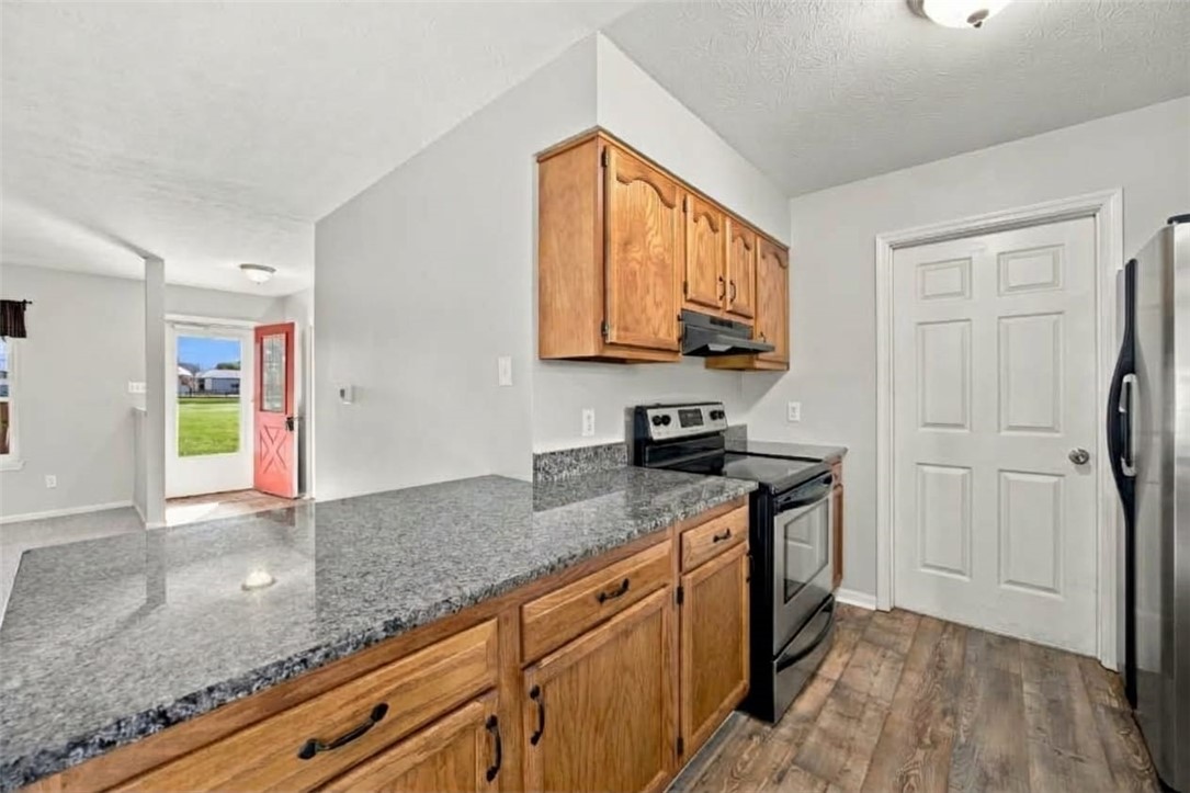 Kitchen with granite counters, wood cabinets, stainless appliances, and an open red door to the lawn.