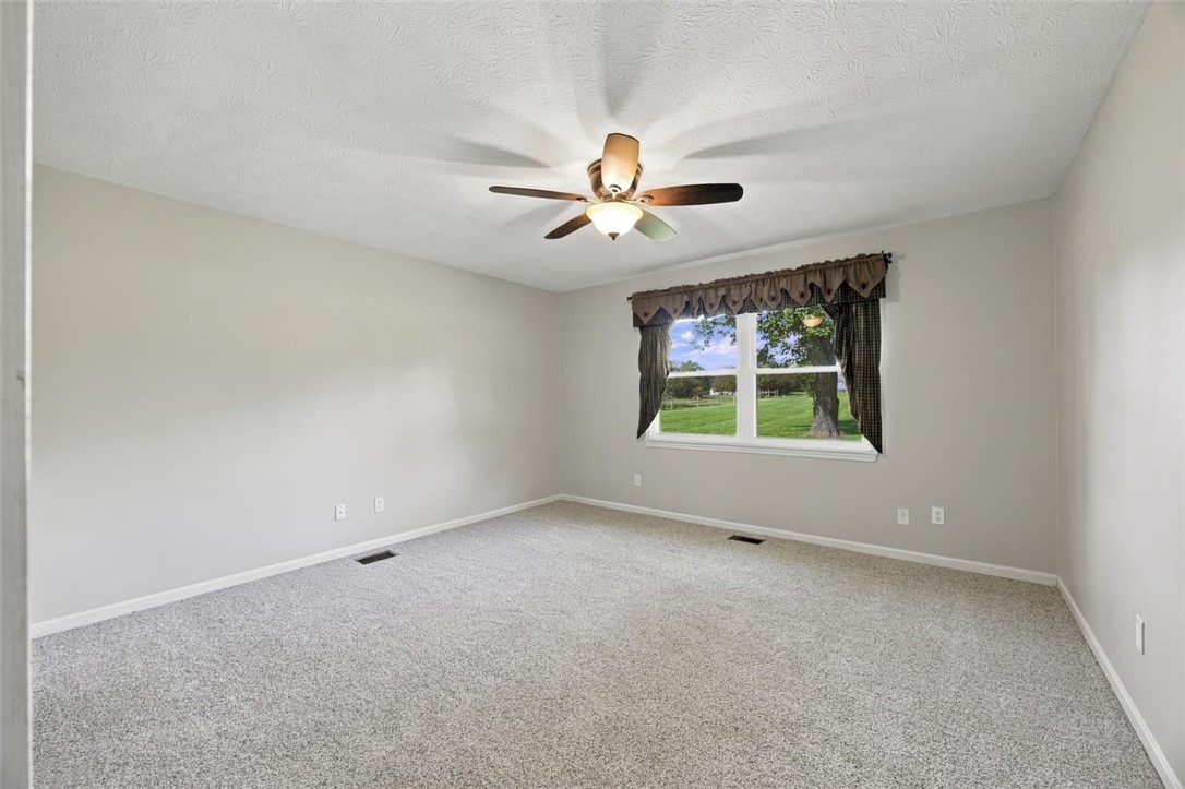 Empty carpeted bedroom with a ceiling fan and a window overlooking a green lawn.