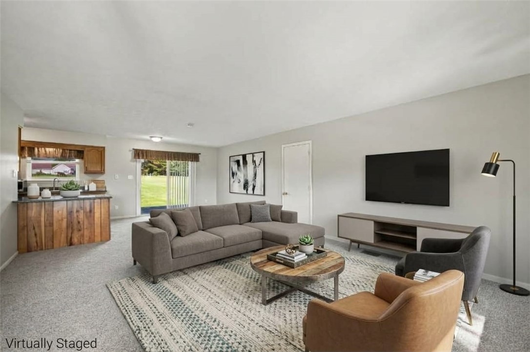 Virtually staged living room with gray sectional, wall-mounted TV, and adjoining kitchen.