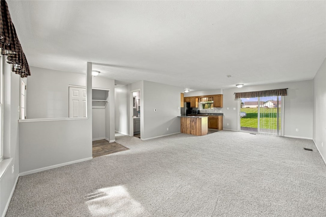 Open living area with gray carpet, wood kitchen cabinets, and sliding doors to the yard.