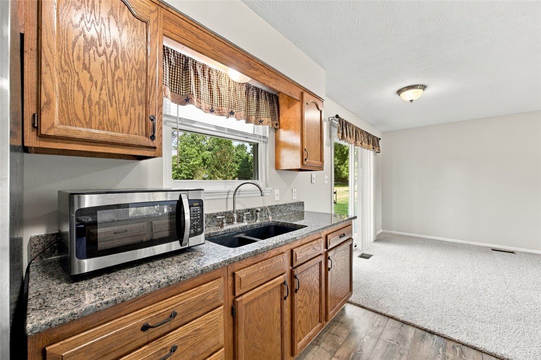 Kitchen with oak cabinets, granite counters, stainless microwave, and sink beside a sliding glass door.