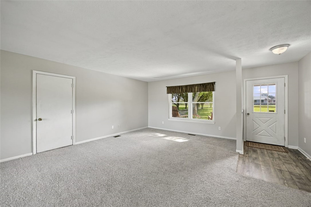 Empty carpeted living room with a large yard-facing window and a white exterior door.