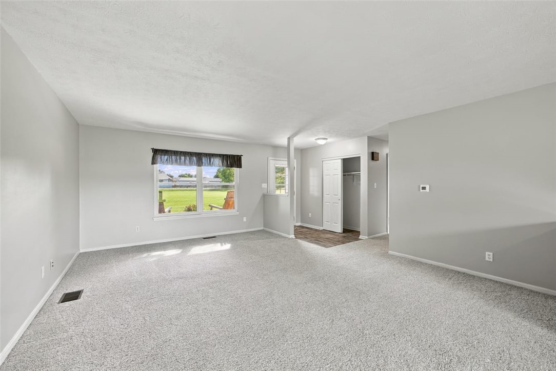Vacant carpeted living room with a large window overlooking a green lawn.