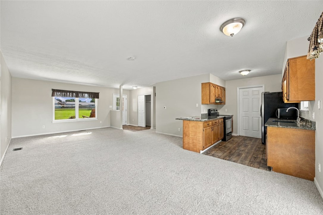Open-plan living room and kitchen with light carpet and wood cabinets.