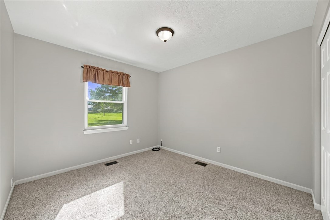 Empty bedroom with beige carpet, gray walls, and a window overlooking a green lawn.