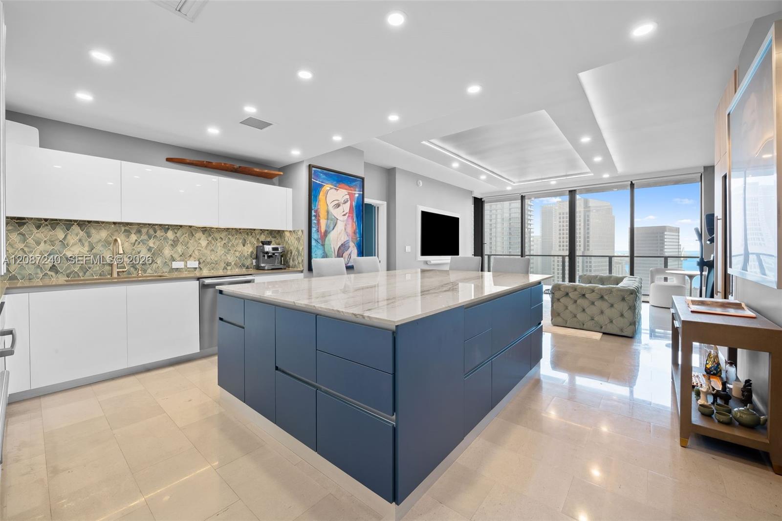 Modern condo kitchen with a blue island, patterned backsplash, and downtown views through floor-to-ceiling windows.