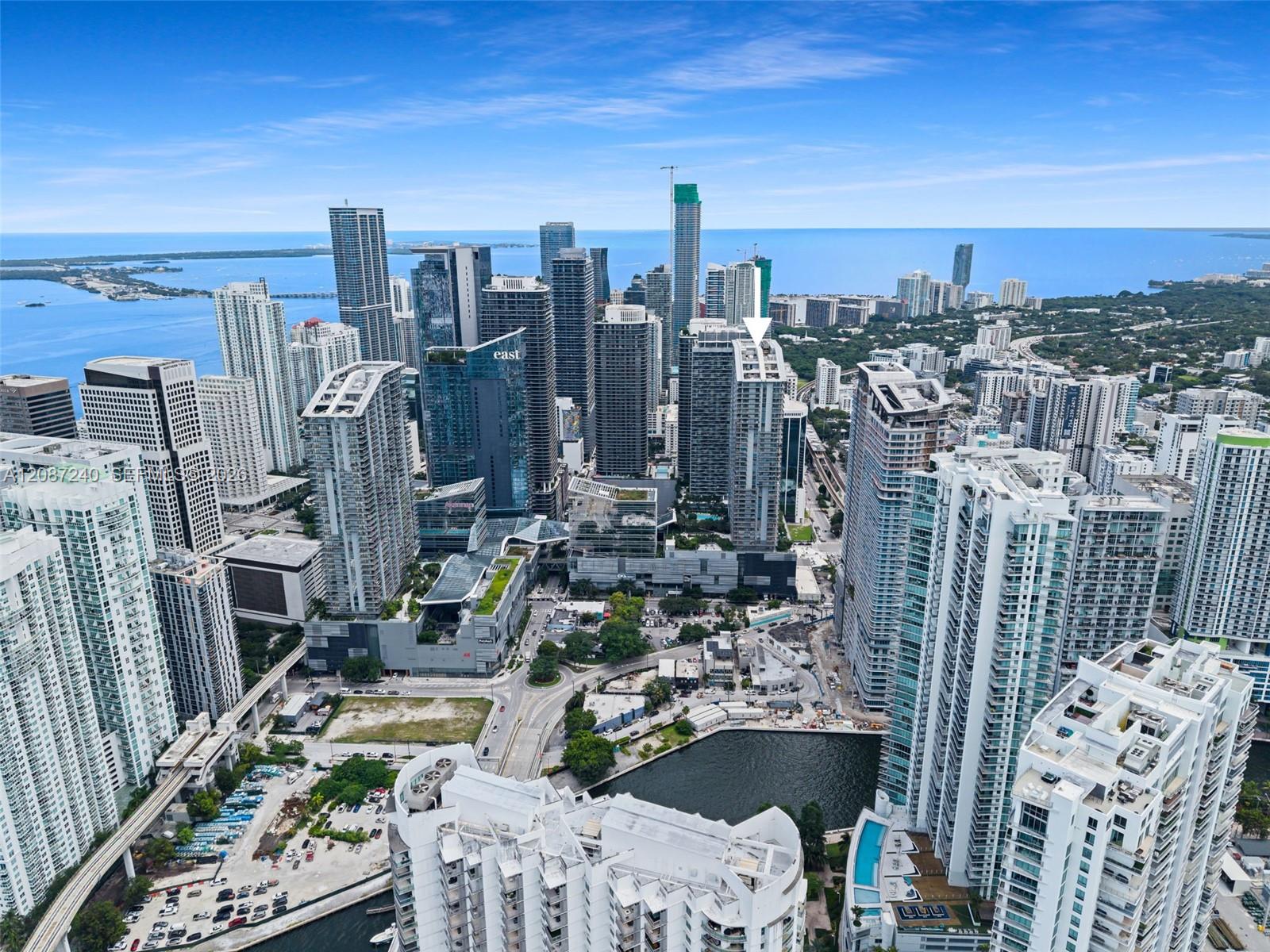 Aerial view of downtown Miami towers and Biscayne Bay, with a white arrow marking one building.