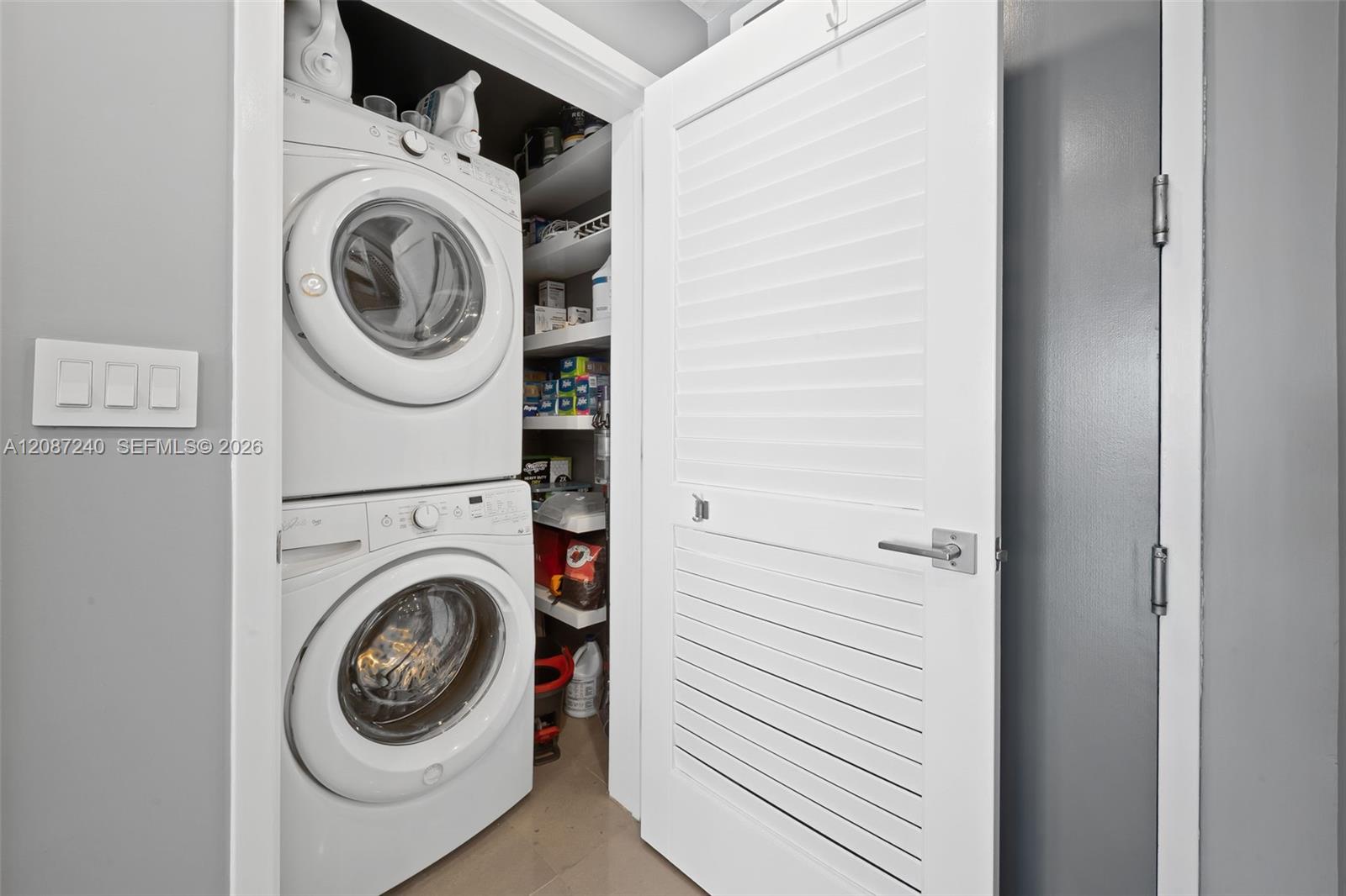 Laundry closet with stacked front-loading washer and dryer beside open storage shelves.