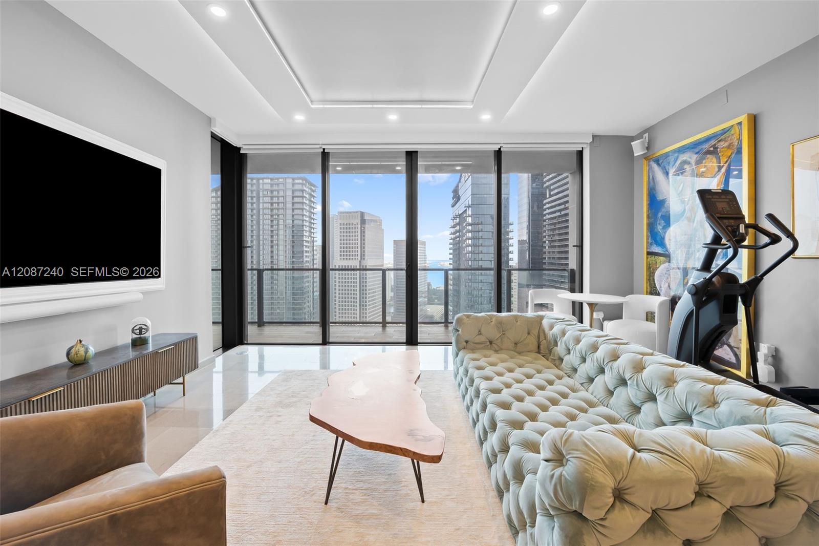 Furnished living room with floor-to-ceiling windows overlooking downtown towers and water.