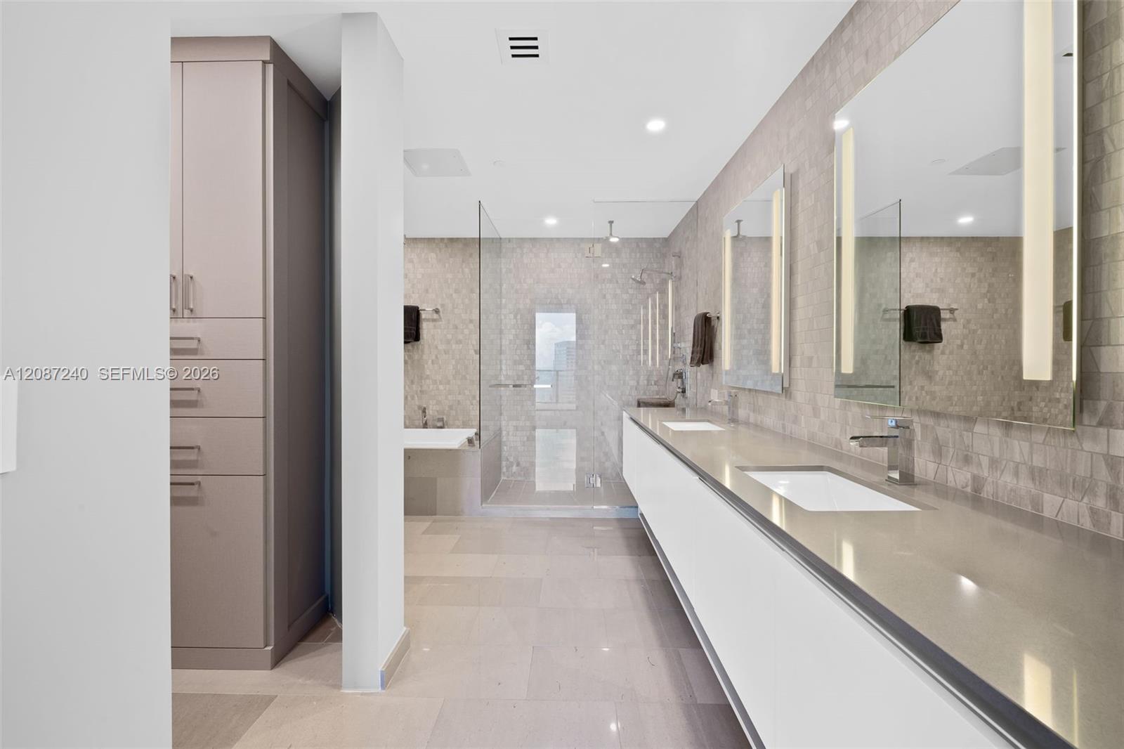 Modern bathroom with a long double vanity, illuminated mirrors, and glass-enclosed shower.