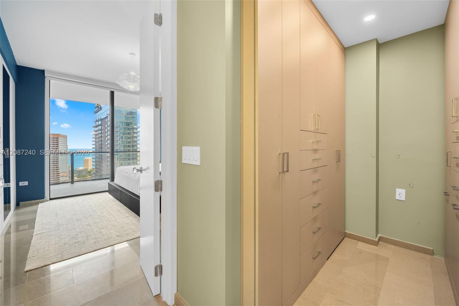 Walk-in closet with built-in cabinetry beside a bedroom overlooking the city and water.