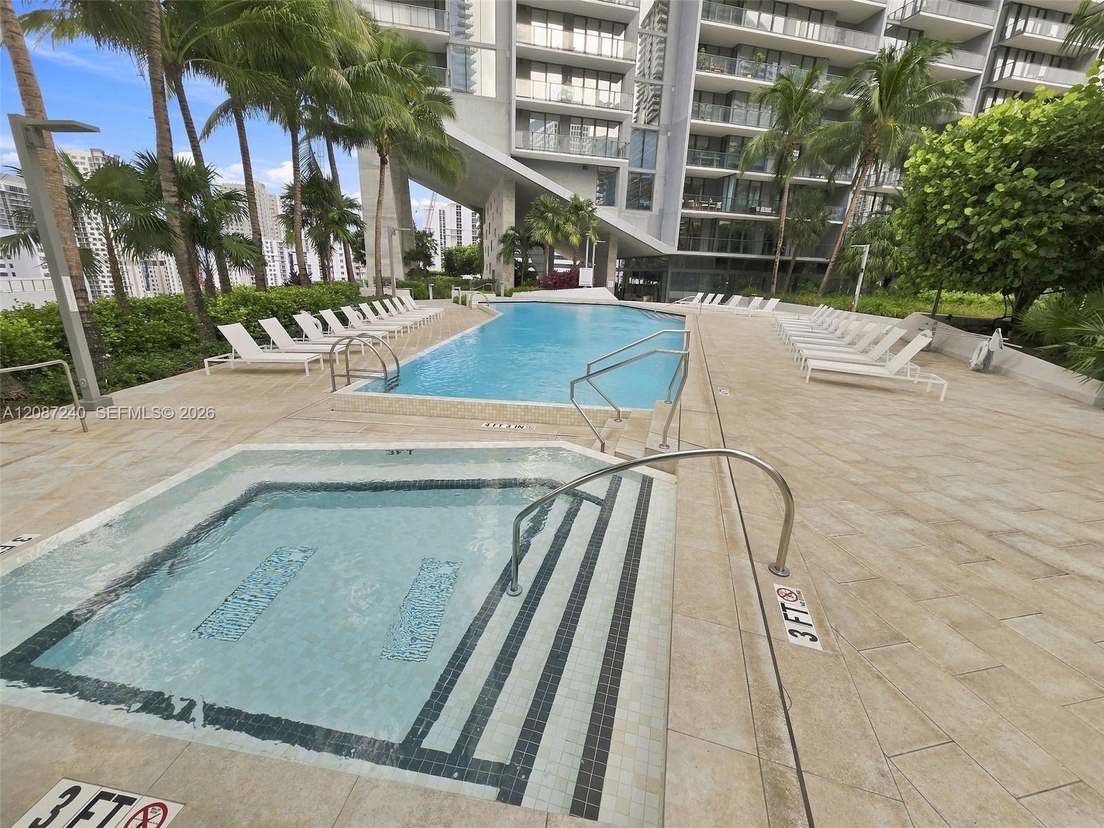 High-rise residential pool with a shallow section, palm trees, and rows of white loungers.