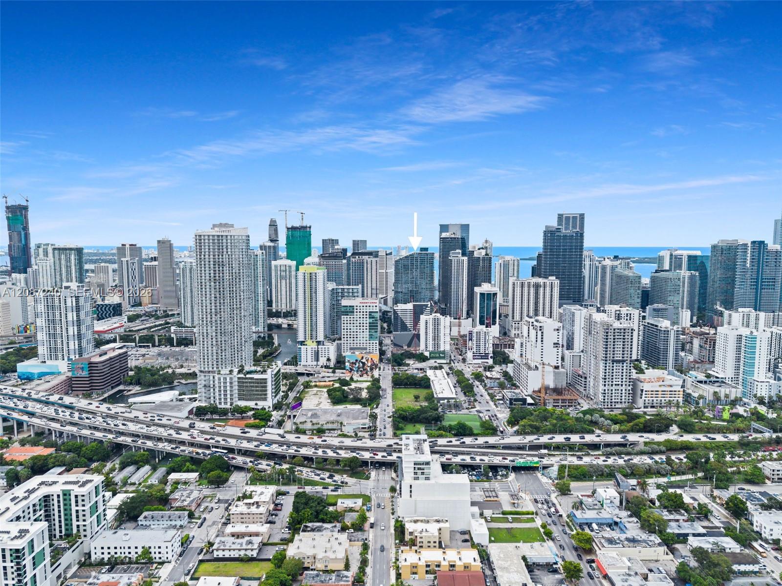 Downtown Miami skyline with an arrow pointing to a high-rise, water beyond and an elevated highway in the foreground.