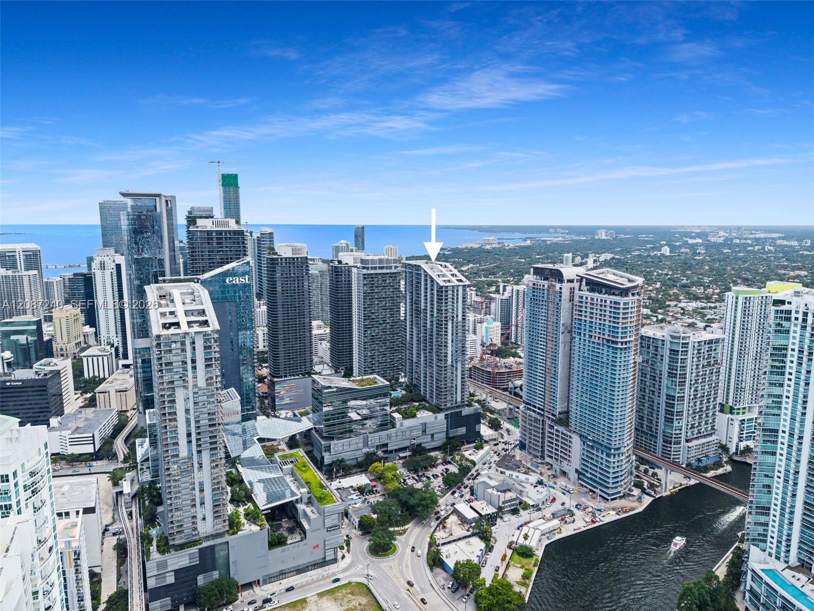 Aerial view of downtown Miami towers, with an arrow marking the condo building and the river in the foreground.