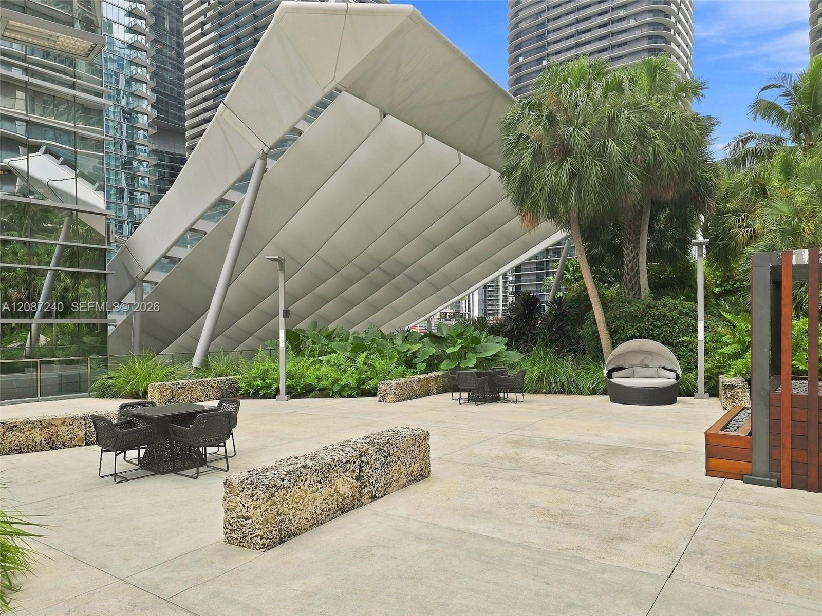Miami high-rise courtyard patio with an angular canopy, palm trees, and outdoor seating.