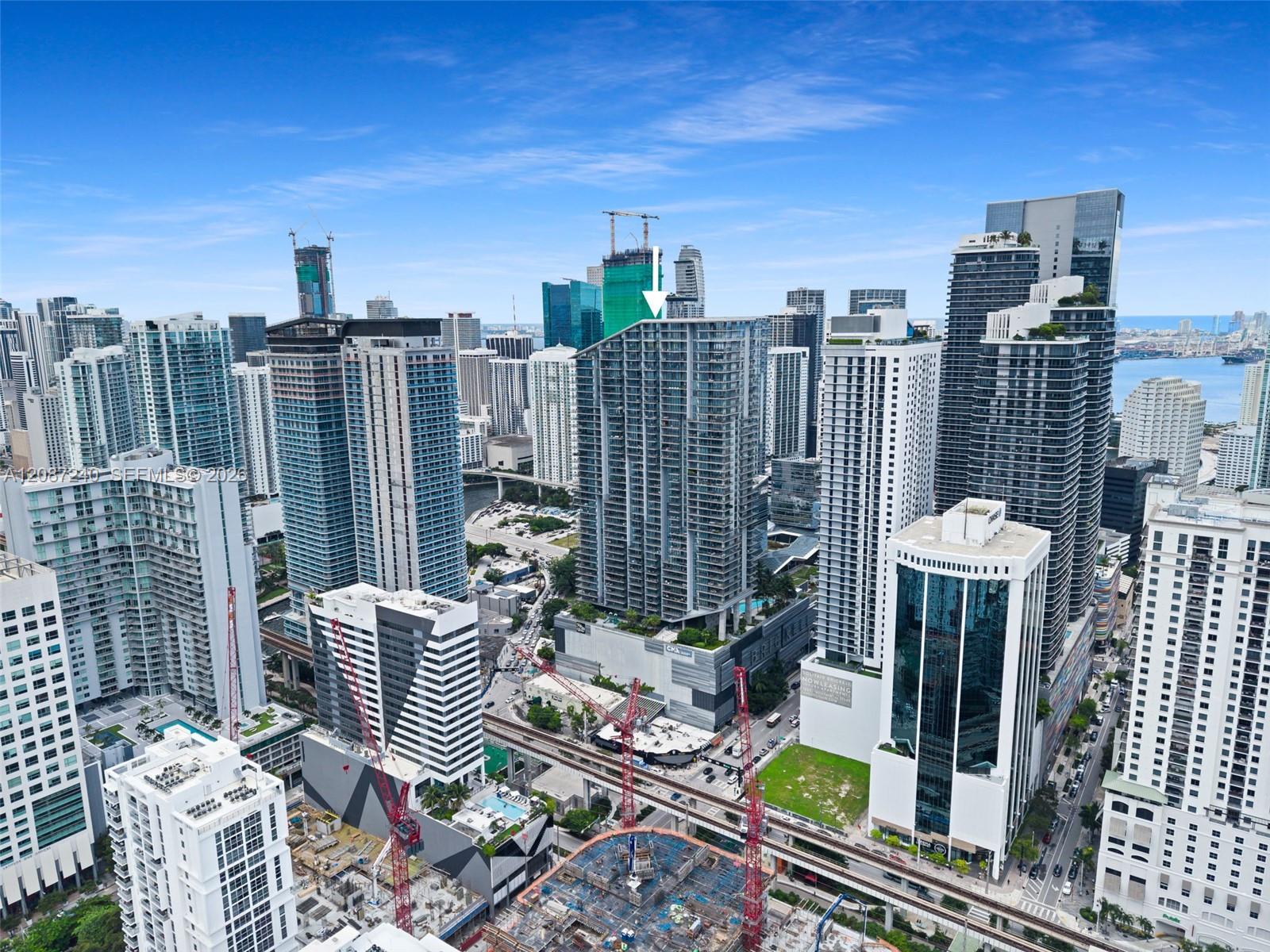 Aerial view of downtown Miami high-rises, with an arrow marking the tower and bay beyond.