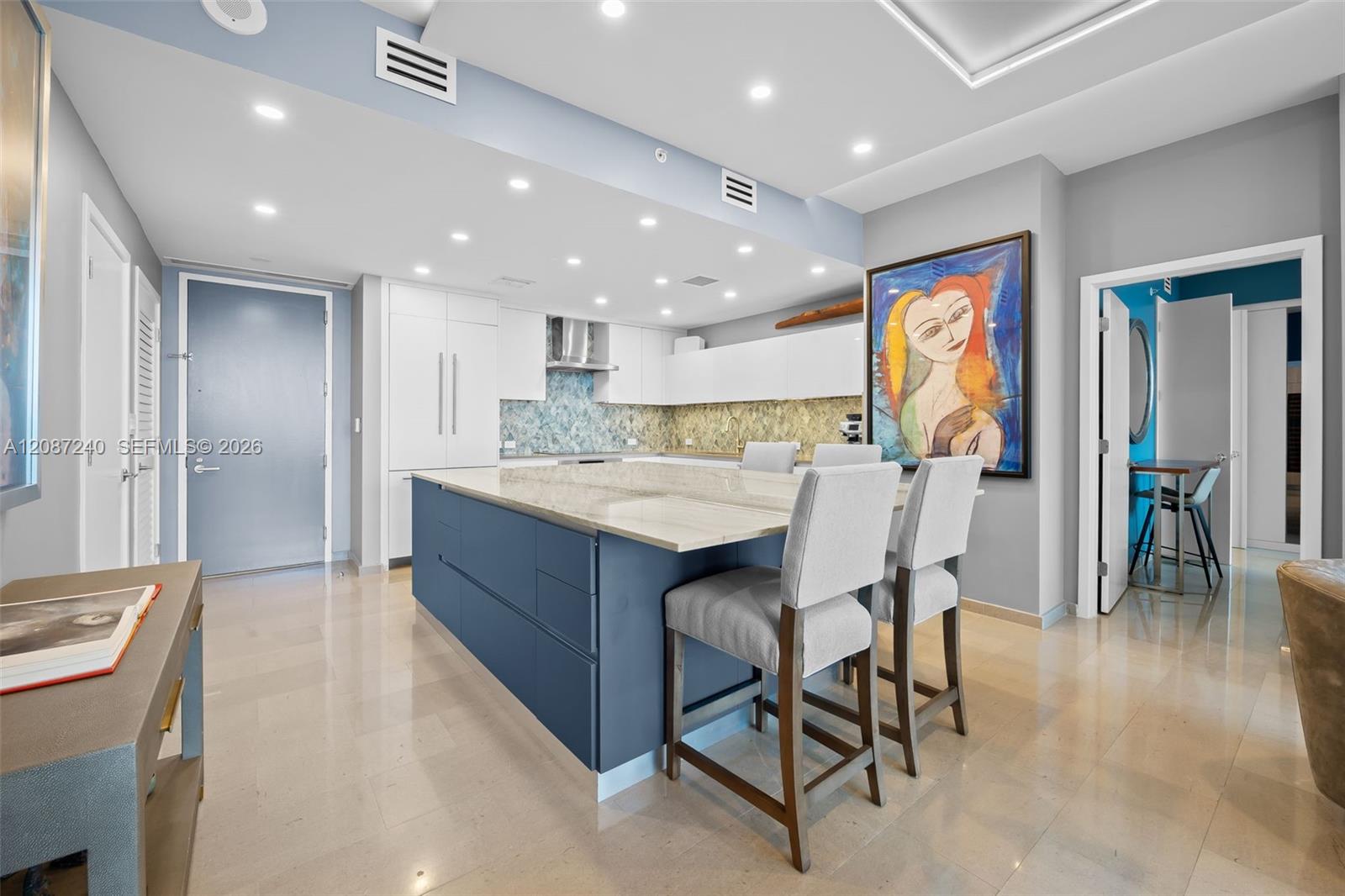 Modern condo kitchen with a navy island, stone countertop, bar stools, and colorful portrait artwork.
