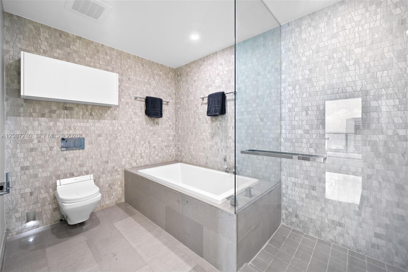 Modern bathroom with a glass-enclosed shower, white bathtub, and pale geometric tile.