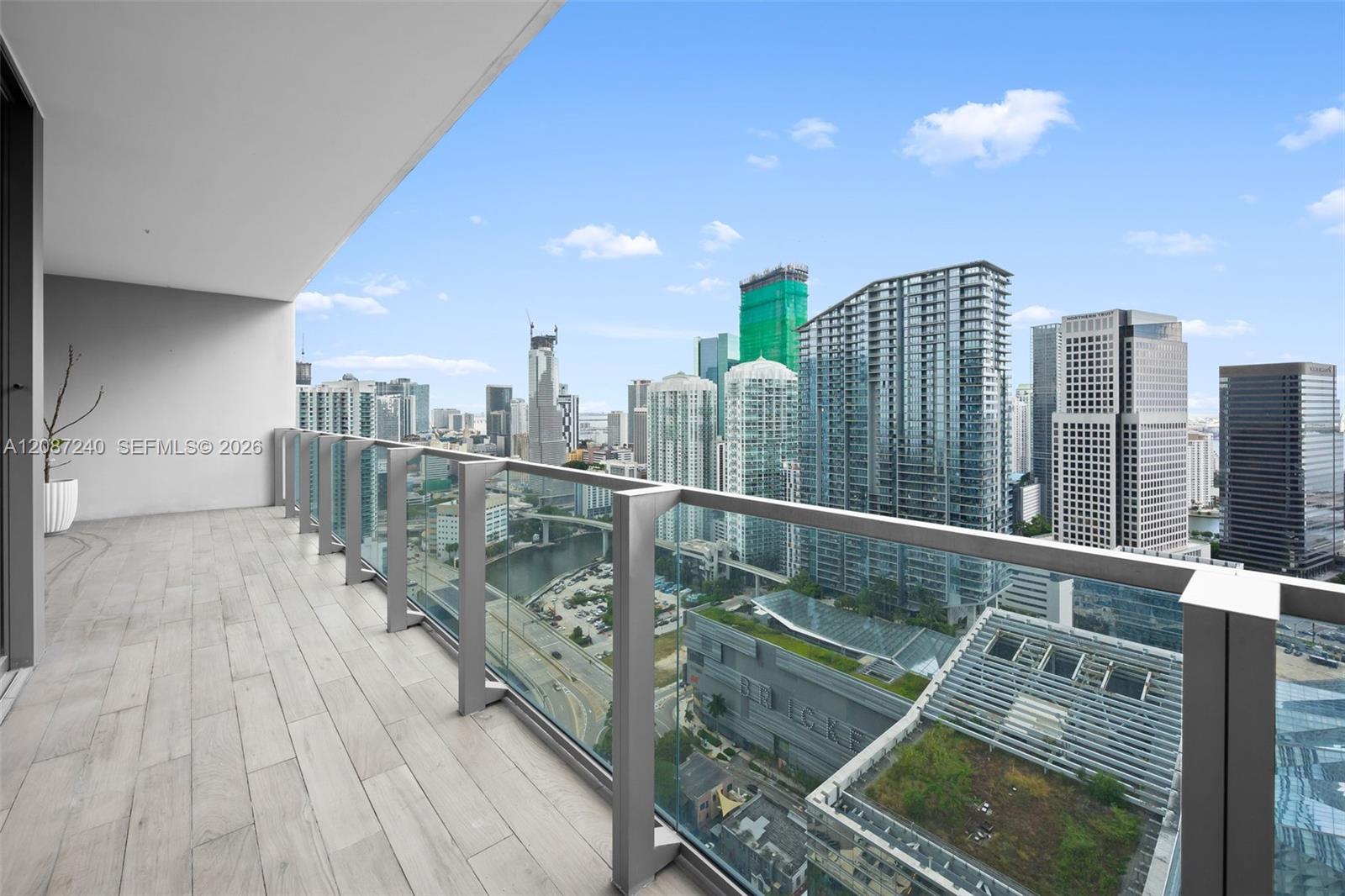 High-rise balcony overlooking downtown Miami towers, with pale tile flooring and a glass railing.