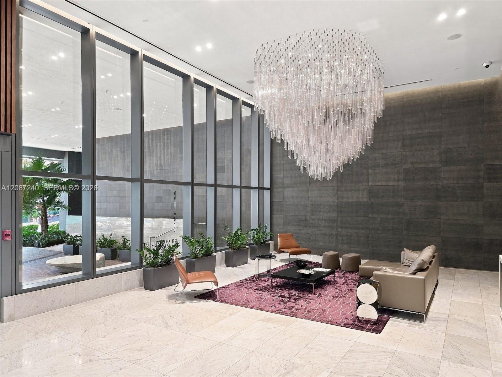 Condominium lobby with a cascading crystal chandelier, tall windows, and a modern seating area.