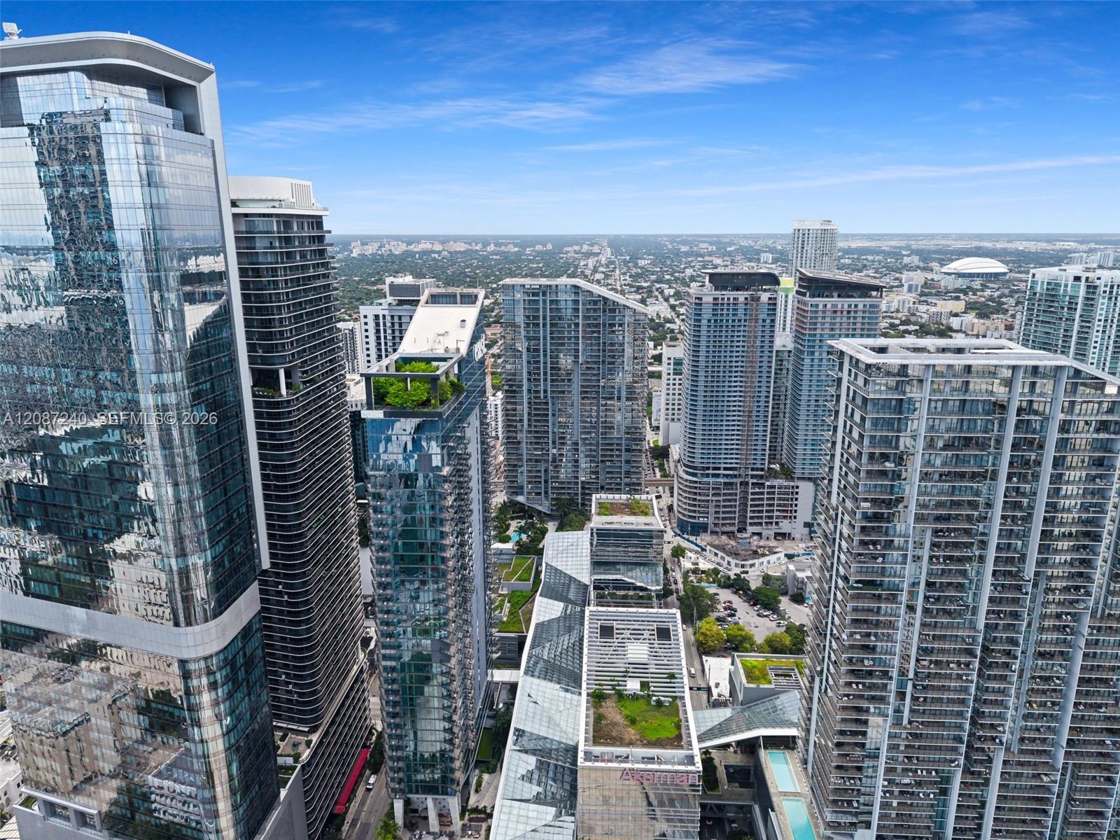Aerial view of downtown Miami’s glass condominium towers and city skyline beneath a blue sky.