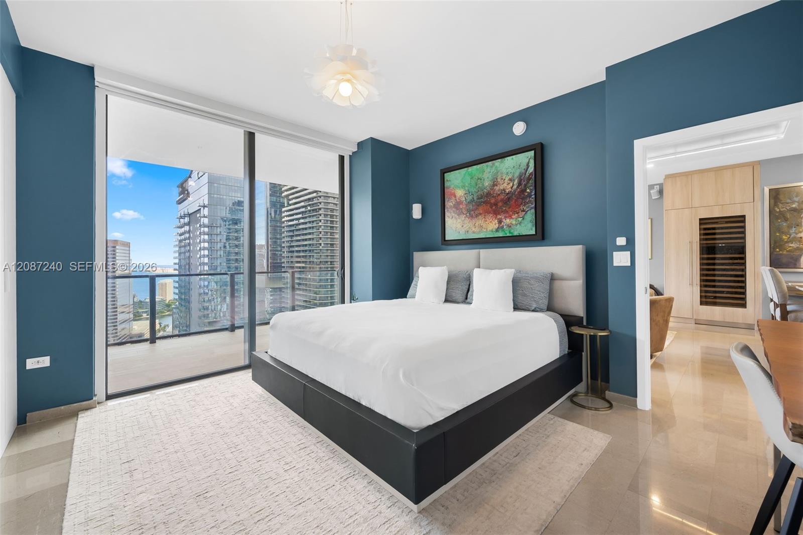 Condominium bedroom with a king bed, teal walls, and balcony views of Miami high-rises and water.
