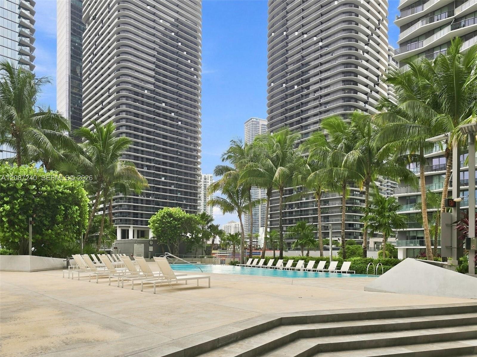 Condominium pool deck with white loungers, palm trees, and curved high-rise towers.