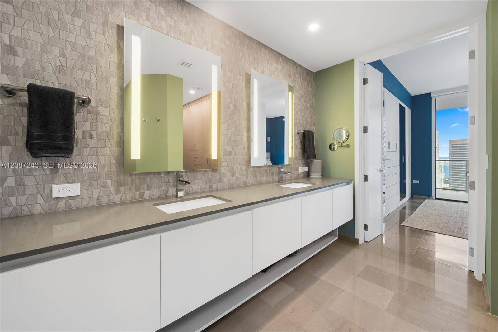 Modern bathroom with a long double vanity, geometric tile, and a doorway toward a balcony view.