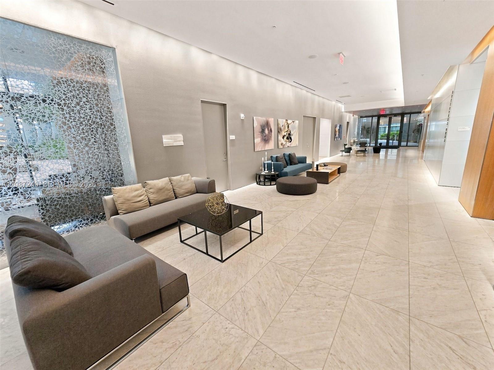 Condominium lobby with marble floors, gray lounge seating, and a patterned glass partition.