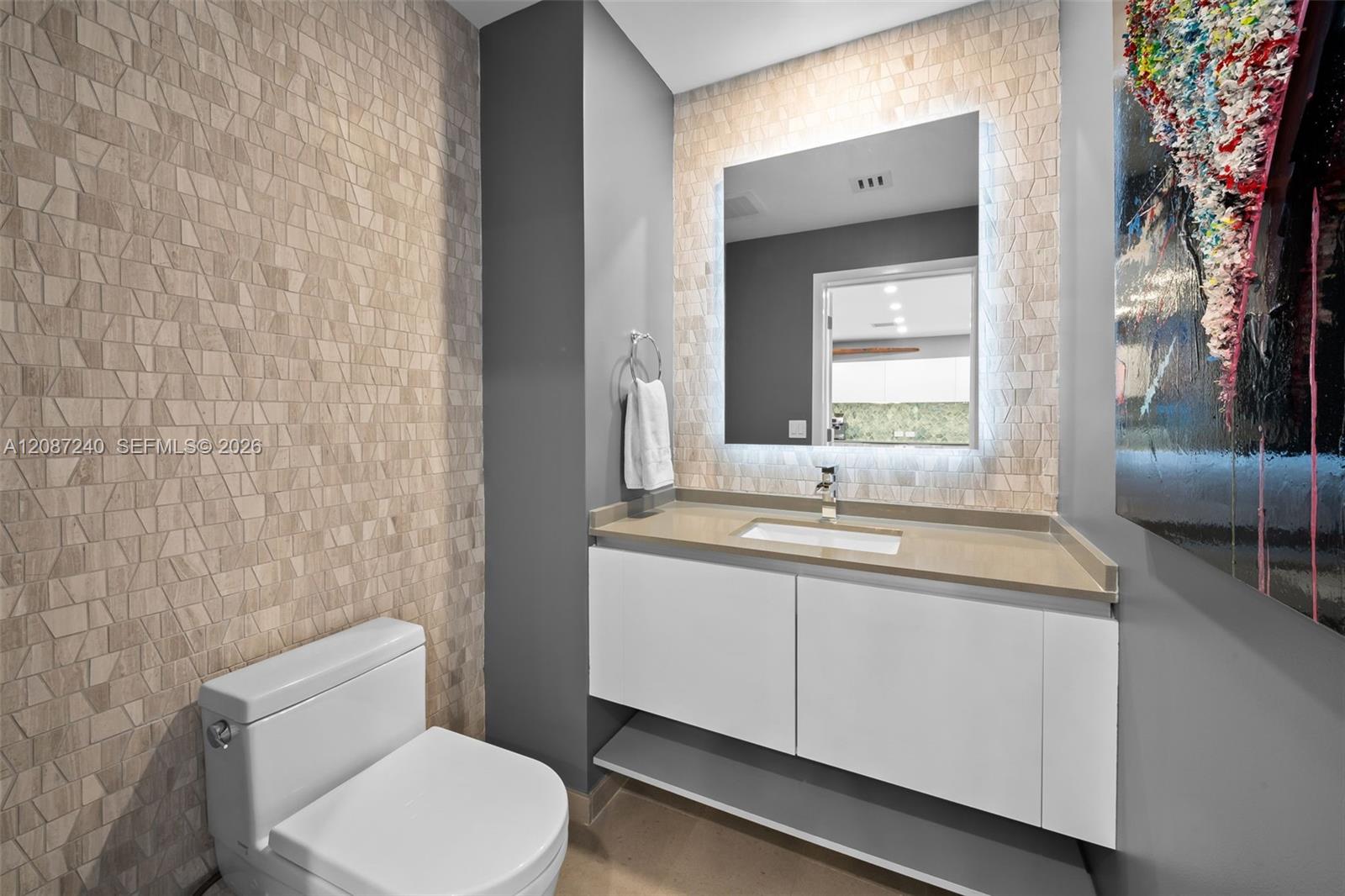 Modern bathroom with floating white vanity, large mirror, geometric tile wall, and colorful abstract artwork.