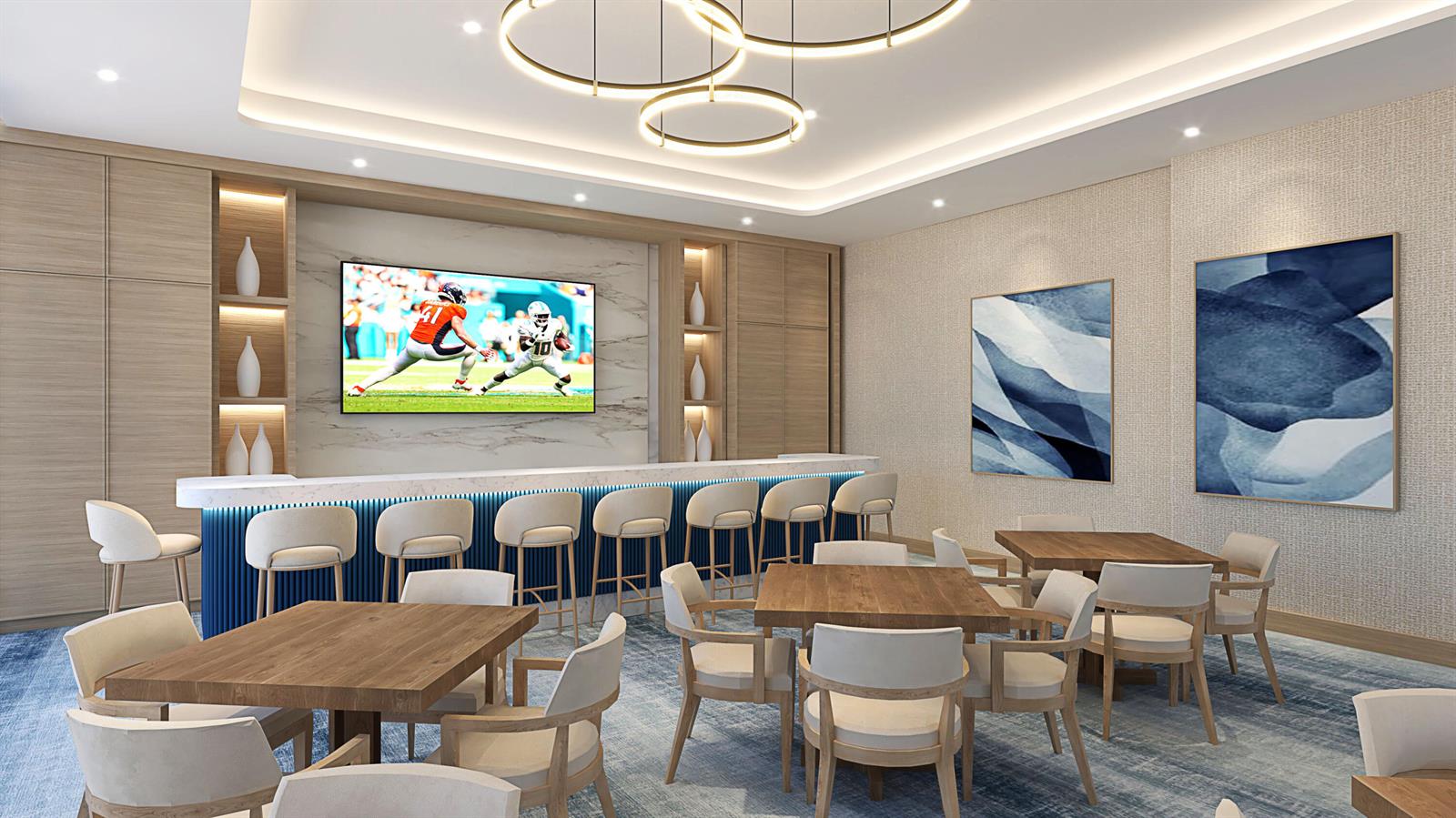 Furnished residential lounge with a long blue-fronted bar, dining tables, and a television.