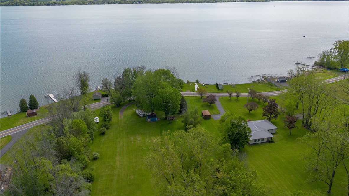 Aerial view of a lakefront property with broad lawns, mature trees, and a shoreline road.