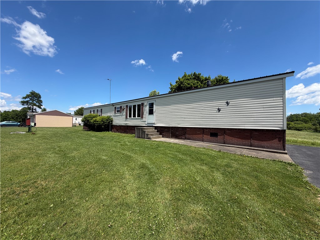 Manufactured home with light siding, concrete entry steps, broad lawn, and a detached outbuilding.