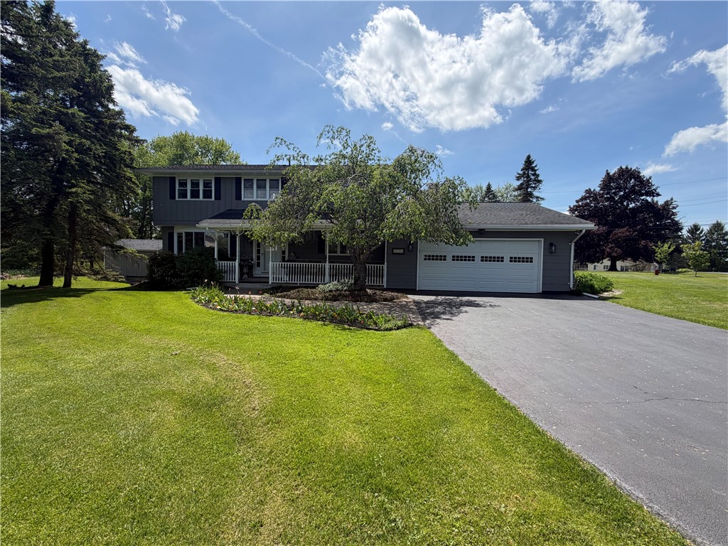 Gray two-story house with a covered porch, attached garage, broad lawn, and mature trees.