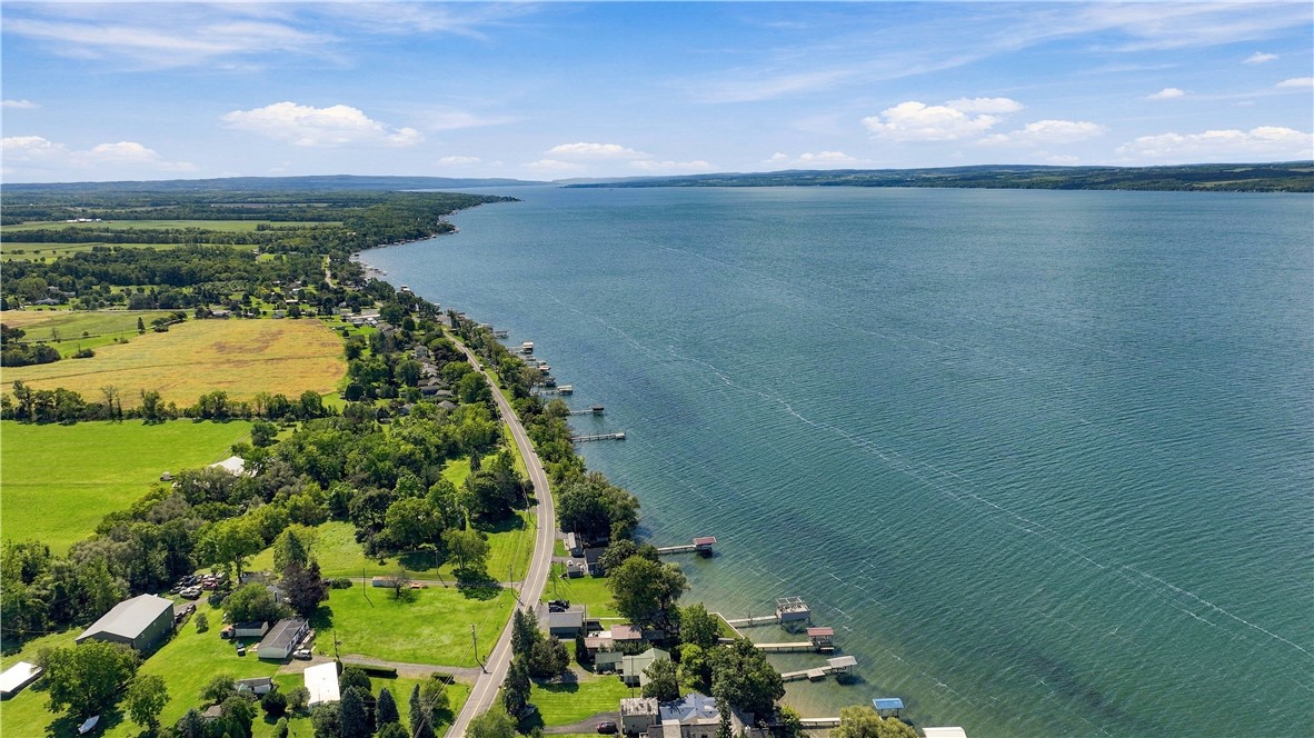 Aerial view of a broad lake and green shoreline, with homes and a road along the water.