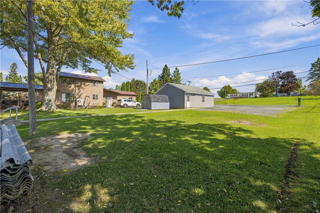 House and detached outbuilding beside a broad lawn shaded by mature trees.