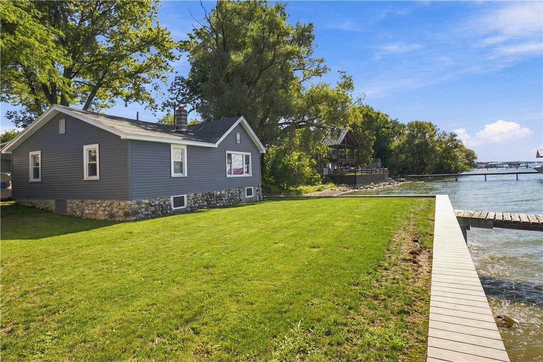 Gray lakeside house with a stone foundation, broad lawn, and dock along the water.