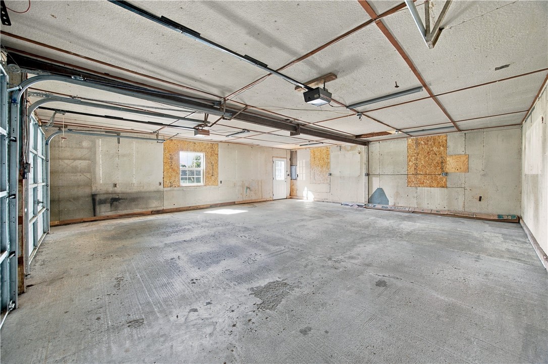 Empty unfinished garage with a wide concrete floor and exposed overhead door tracks.