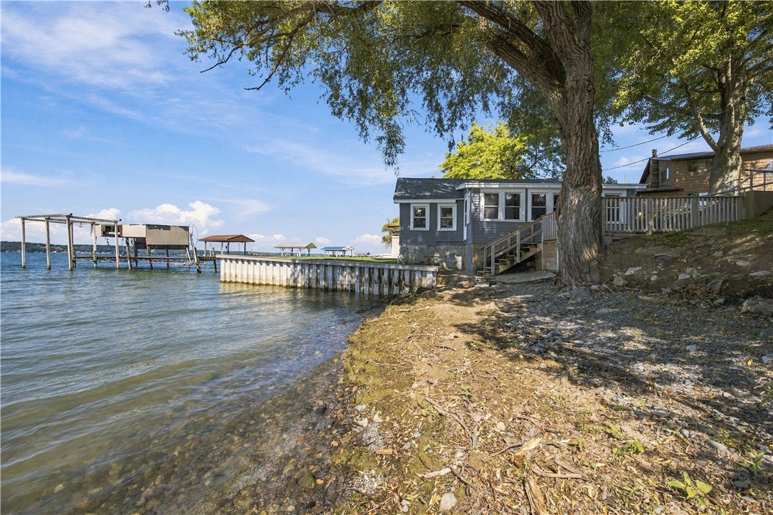 Lakeside house with a raised deck, broad dock, and rocky shoreline under a large tree.