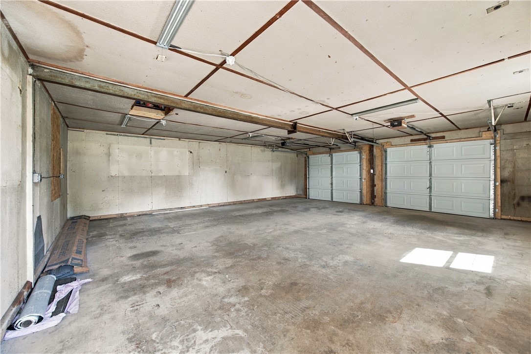 Vacant two-car garage with white overhead doors, a concrete floor, and exposed ceiling framing.