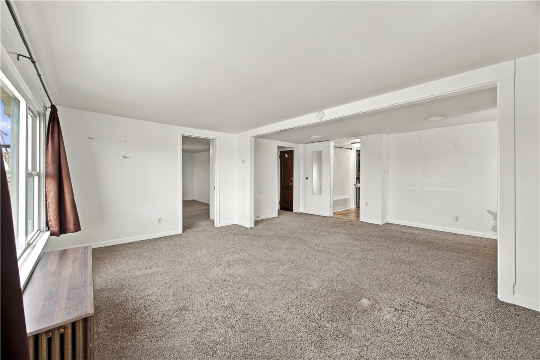 Vacant carpeted living room with a large curtained window and open doorways.