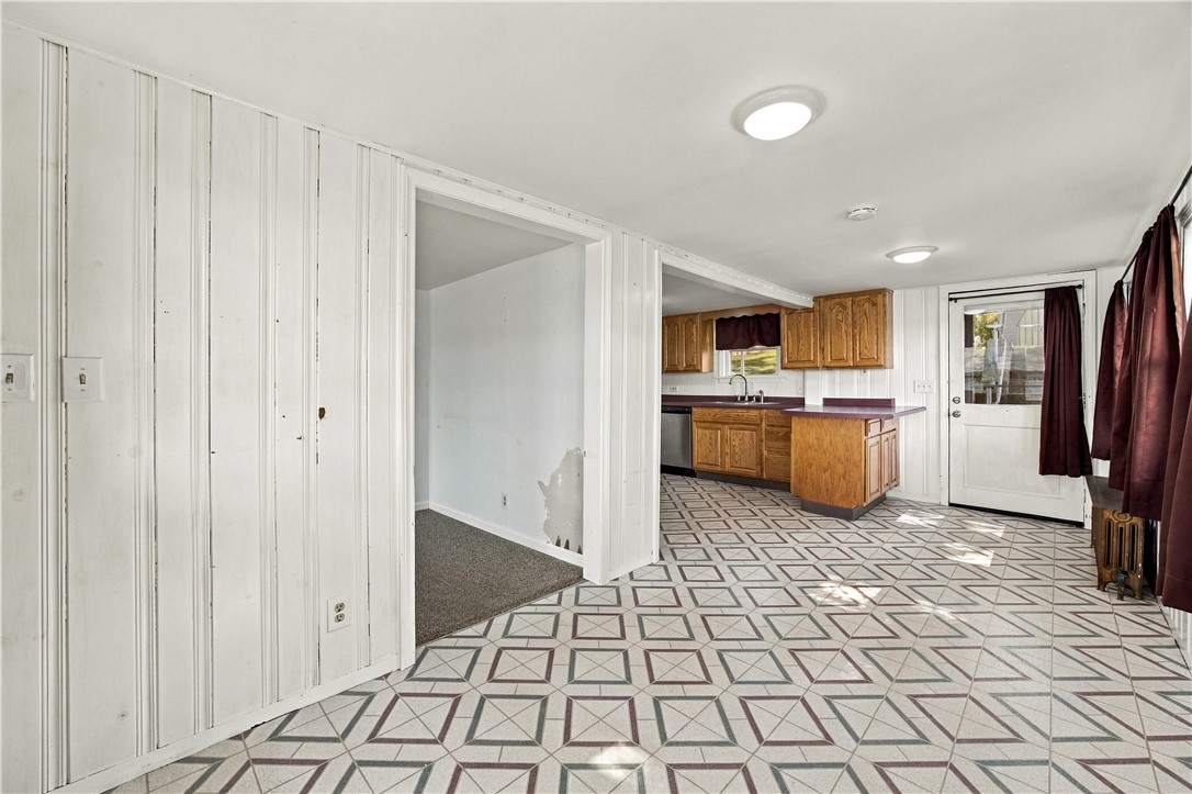 Kitchen with wood cabinets and peninsula, geometric tile floor, and adjoining carpeted room.
