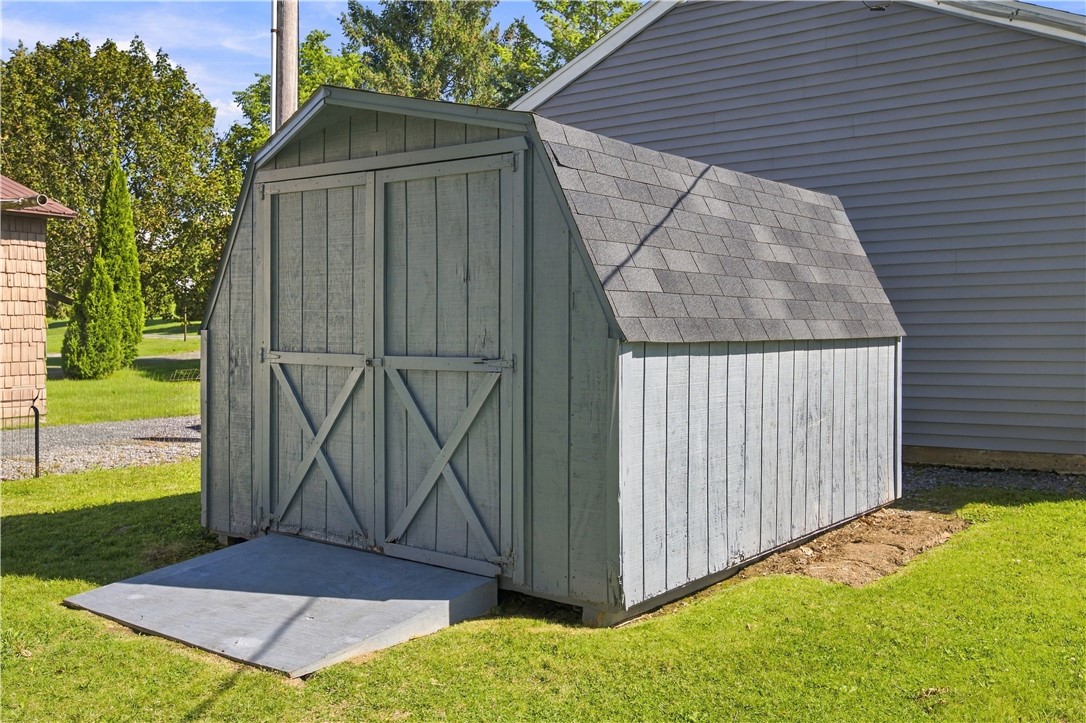 Gray wooden storage shed with cross-braced double doors and a concrete ramp beside a house.