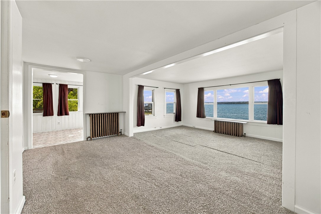 Empty living room with broad lake views through large windows and a doorway to a tiled room.