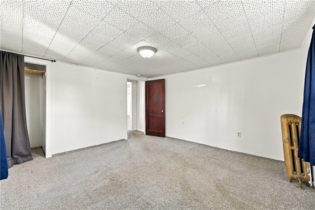 Empty carpeted room with a dark wooden door and brass radiator.