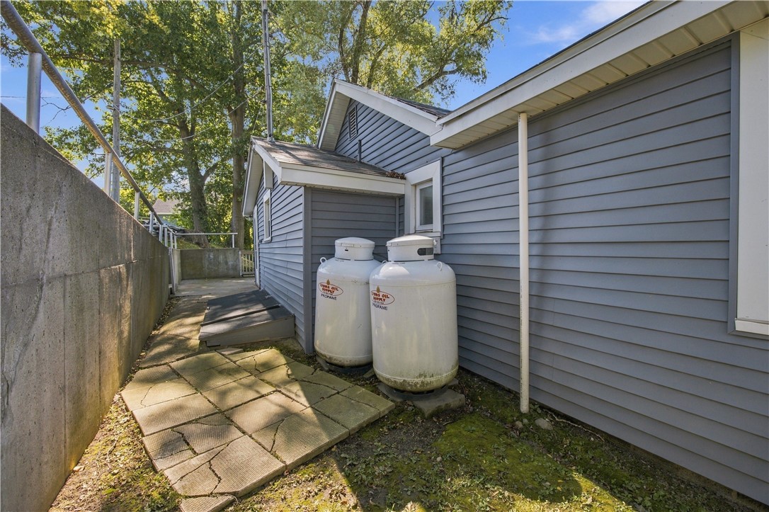 Gray-sided house exterior with two propane tanks beside a narrow walkway and concrete retaining wall.