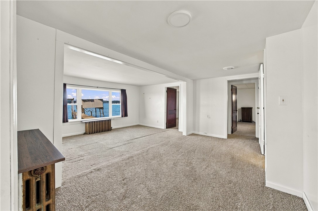 Unfurnished living room with a large lake-facing window and beige carpeting.